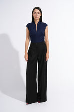 Load image into Gallery viewer, A woman stands against a plain white studio background wearing a navy blue sleeveless top with a split neckline and black wide-leg trousers.