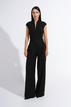 Load image into Gallery viewer, A woman modeling a black sleeveless jumpsuit with a split neckline, high-waisted wide-leg pants, and a matching waist belt, photographed against a plain white studio background.