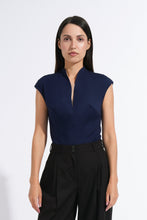 Load image into Gallery viewer, A woman stands against a plain white studio background wearing a navy blue sleeveless top with a split neckline and black wide-leg trousers.
