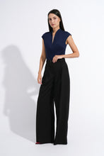 Load image into Gallery viewer, A woman modeling a sleeveless navy blue top with a deep V-neckline and black wide-leg trousers, standing against a white studio background with a soft shadow.
